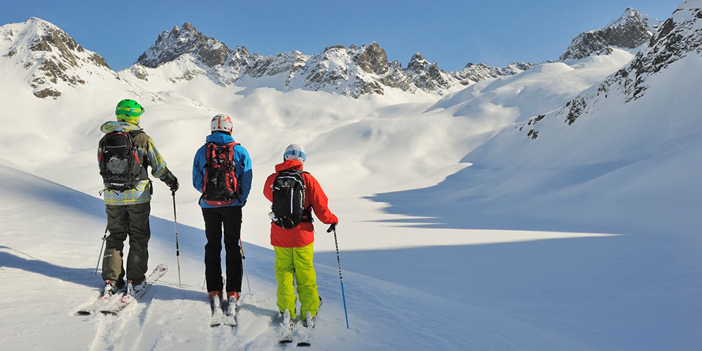 Drei Skifahrer am sonnigen Tiefschneehang in St. Anton am Arlberg
