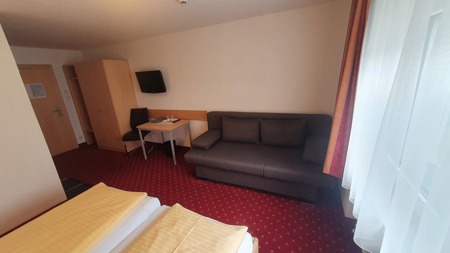 Mehrbettzimmer mit Couch und Fernseher im Hotel Dorfblick